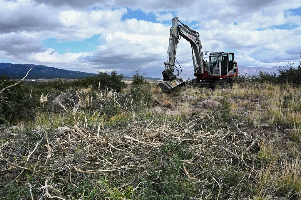 Tracked excavator fitted with a mulching head working over cleared brush